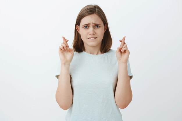 Nervosa esperançosa mulher bonita com uma linda orelha abaulada mordendo o lábio inferior ansiosamente e franzindo a testa parecendo intensa enquanto espera notícias importantes cruzando os dedos por boa sorte, fazendo desejo