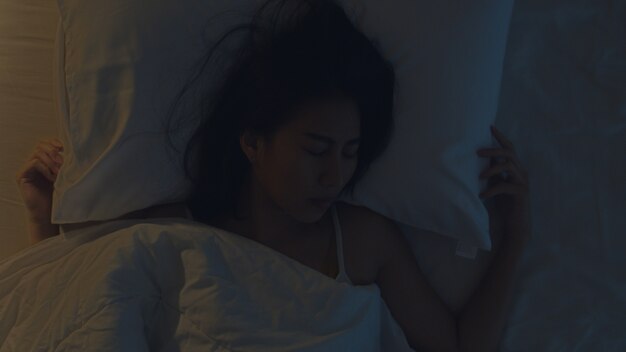 Nervosa jovem mulher asiática, tendo um pesadelo deitado na cama em seu quarto em casa no meio da noite. Sofrendo de dor de cabeça ou enxaqueca, insônia, apneia do sono ou estresse. Vista superior.