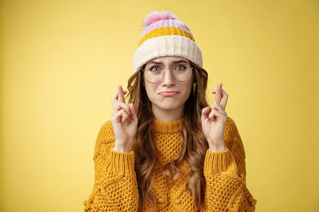 Nervoso, inseguro, inseguro, fofa, nerd, estudante, universitário, usando óculos, amuando, chorando, choramingando, dedos cruzados preocupados, boa sorte rezando sonho tornado realidade em pé fundo amarelo intenso