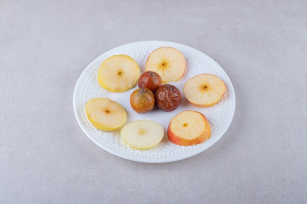 Nêspera e maçãs fatiadas no prato, no mármore.