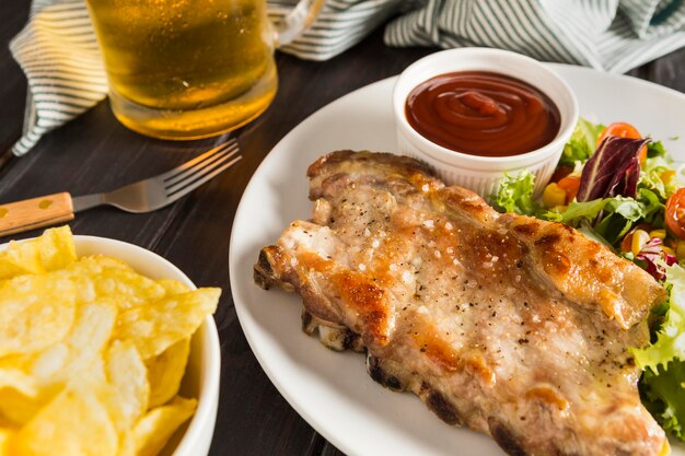 Ângulo alto de bife no prato com molho e copo de cerveja