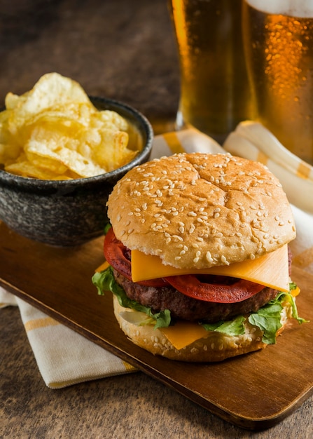 Ângulo alto de copos de cerveja com cheeseburger e batatas fritas