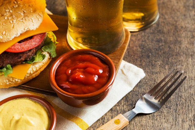 Ângulo alto de copos de cerveja com cheeseburger e molho