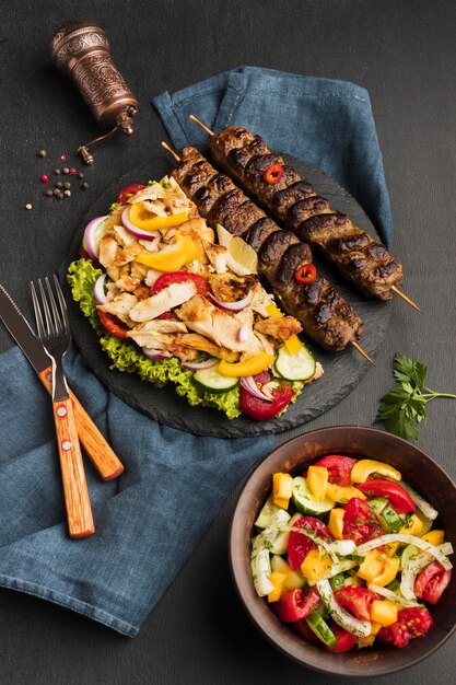 Ângulo alto do saboroso kebab na lousa com outro prato e talheres