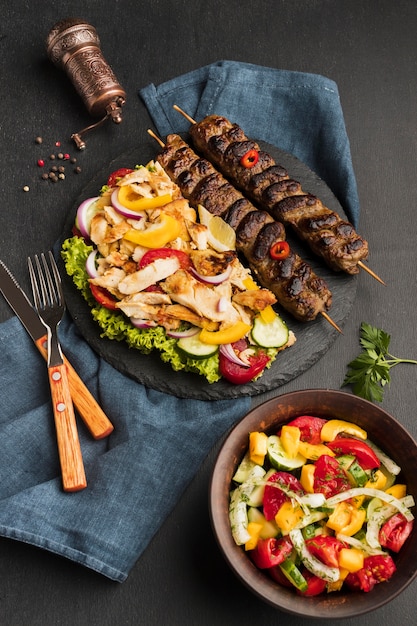 Ângulo alto do saboroso kebab na lousa com outro prato e talheres