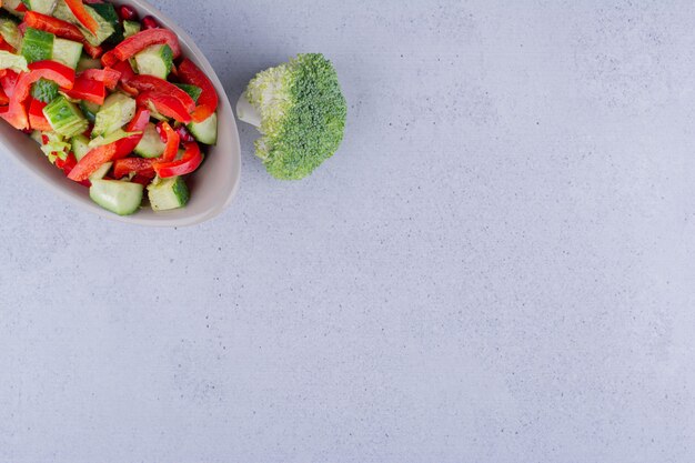 Único pedaço de brócolis ao lado de uma tigela cinza de salada mista no fundo de mármore. Foto de alta qualidade