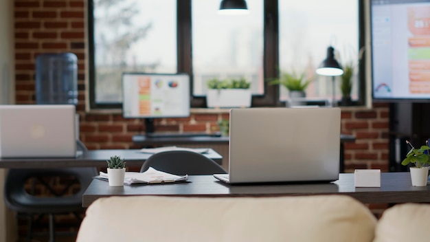 Ninguém na mesa de escritório com documentos gráficos e laptop, usado pelo funcionário da empresa para planejar o crescimento financeiro. Local de trabalho vazio com computadores, tecnologia e estatísticas de marketing na tela.