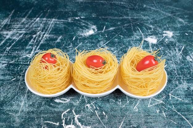 Ninhos de espaguete cru com tomate na chapa branca. Foto de alta qualidade