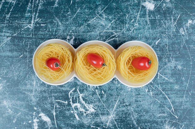 Ninhos de espaguete cru com tomates no espaço azul.