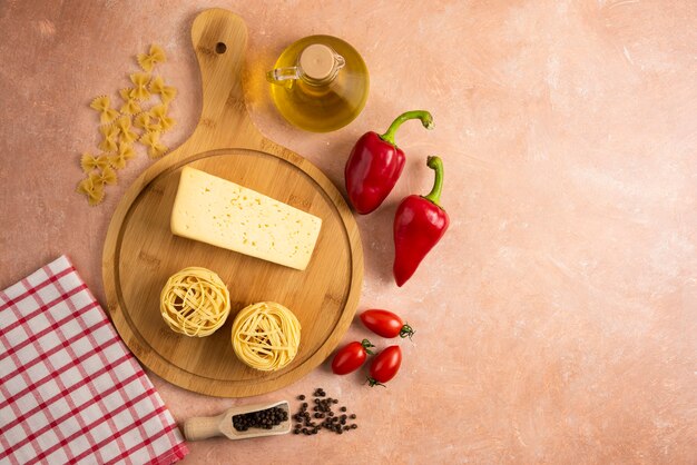 Ninhos de espaguete cru e queijo na placa de madeira com legumes.