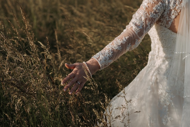 Noiva caminhando em um campo de trigo usando um lindo vestido de noiva e uma pulseira de pérolas