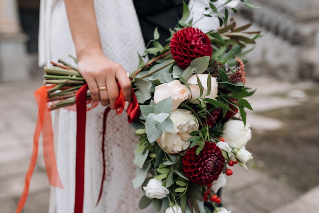 Noiva de vestido branco contém rico buquê de flores vermelhas e brancas