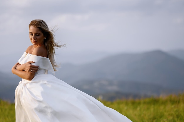 Noiva de vestido branco em pé no prado com vista para as montanhas
