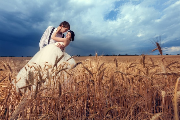 Noiva e noivo no campo de trigo com céu dramático. Apenas casal. Fotografia e fotos de casamento. Família jovem feliz