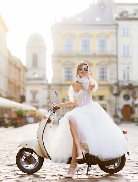 Noiva em vestido de noiva e óculos de sol posando na scooter