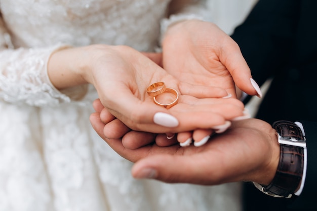 Noivo segura as mãos da noiva, onde estão dois anéis de casamento