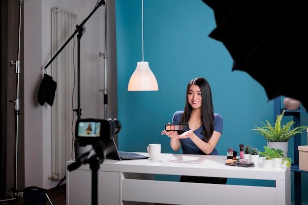 Foto grátis nos bastidores do influenciador asiático filmando revisão de paleta de maquiagem gravando tutorial de beleza para conteúdo de mídia social. criador de vlogger transmitindo produtos cosméticos usando equipamento de transmissão