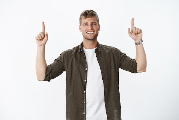 Nós somos campeões pertencem ao topo Retrato de um homem europeu loiro feliz e bonito satisfeito com um sorriso branco perfeito sorrindo como apontando para cima com as mãos levantadas mostrando algo incrível e legal