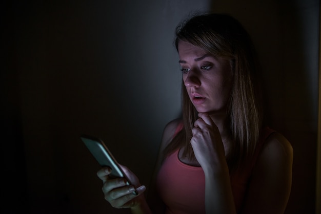 Notícias tristes. A jovem virada com telefone celular lê a mensagem. Retrato noturno na casa