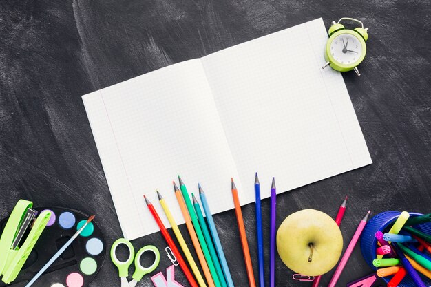 Novo caderno branco ao lado de artigos de papelaria brilhante e apple em fundo cinza