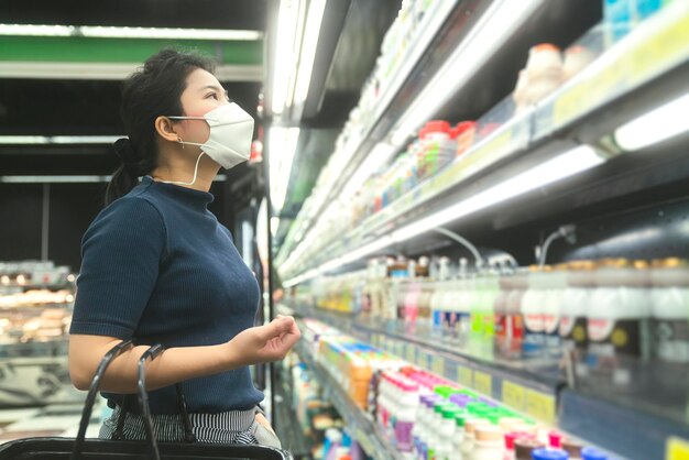 Novo normal após epidemia de covid jovem mulher asiática inteligente comprando novo estilo de vida no supermercado com protetor facial ou proteção de máscara escolher produtos de consumo novo estilo de vida normal