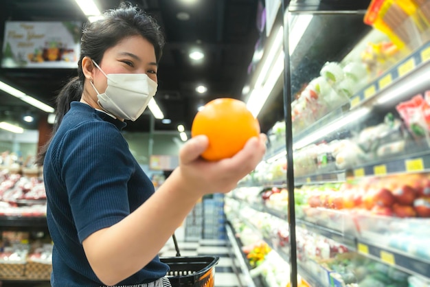 Novo normal após epidemia de covid jovem mulher asiática inteligente comprando novo estilo de vida no supermercado com protetor facial ou proteção de máscara escolher produtos de consumo novo estilo de vida normal