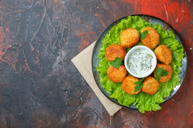 Foto grátis nuggets de frango com alface e molho de cima no prato na mesa escura com espaço de cópia