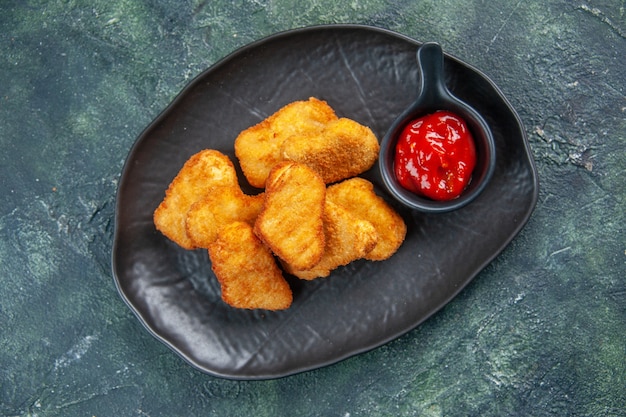 Nuggets de frango deliciosos e ketchup em pratos pretos em superfície escura com espaço livre em close-up