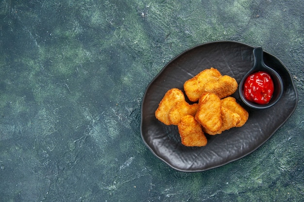 Nuggets de frango saborosos e ketchup em placa preta do lado esquerdo em superfície escura