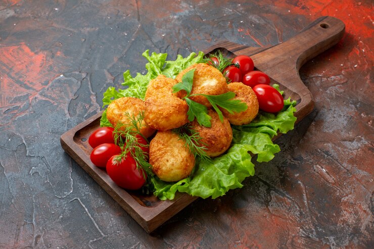 Foto grátis nuggets de frango, tomate cereja, alface, vista inferior, numa tábua, na mesa escura, com espaço de cópia