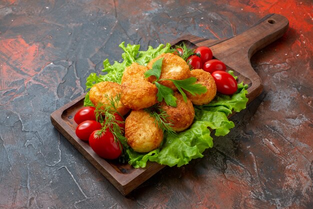 Nuggets de frango, tomate cereja, alface, vista inferior, numa tábua, na mesa escura, com espaço de cópia