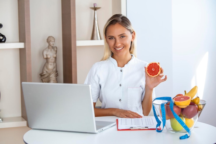 Foto grátis nutricionista sorridente em seu escritório, ela está mostrando o conceito de saúde e dieta de vegetais e frutas saudáveis nutricionista feminina com frutas trabalhando em sua mesa