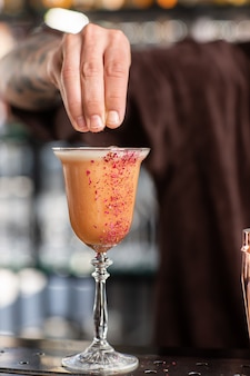 O barman profissional decorou um cocktail alcoólico de laranja com rosa vermelha. visão turva.