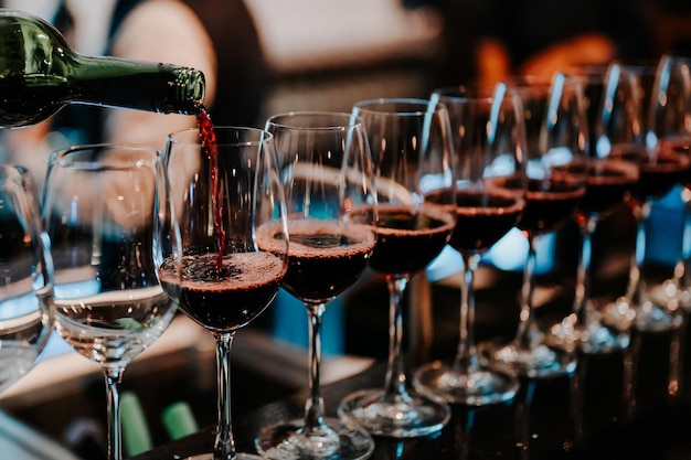 O barman serve vinho tinto em taças no bar. sommelier masculino servindo vinho tinto em taças de vinho de cabo longo.