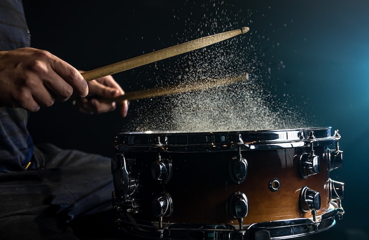 Foto grátis o baterista usando baquetas batendo na tarola com salpicos de água no fundo preto sob a iluminação do estúdio close-up.