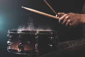 O baterista usando baquetas batendo na tarola com salpicos de água no fundo preto sob a iluminação do estúdio close-up.