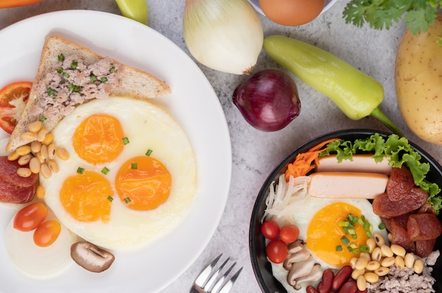 O café da manhã consiste em ovos fritos, lingüiça, carne de porco picada, pão, feijão vermelho e soja em um prato branco.