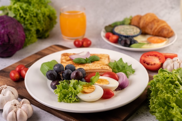 O café da manhã consiste em pão, ovos cozidos, molho para salada de uva preta, tomate e cebola fatiada.