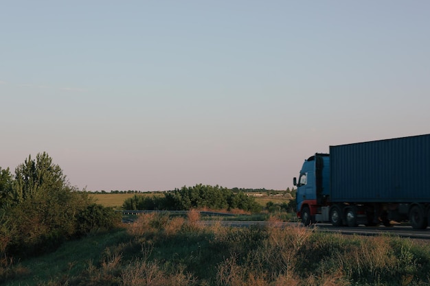 O caminhão está dirigindo na rodovia entre os campos no fundo do céu azul