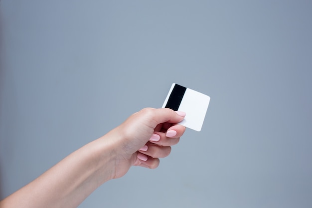 Foto grátis o cartão em uma mão feminina está em um fundo cinza
