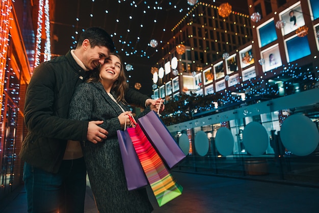 O casal feliz com sacolas de compras curtindo a noite na cidade