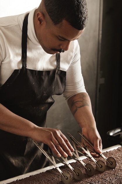 O chef profissional negro usa um separador vintage para marcar as peças em um bolo de chocolate recém-assado