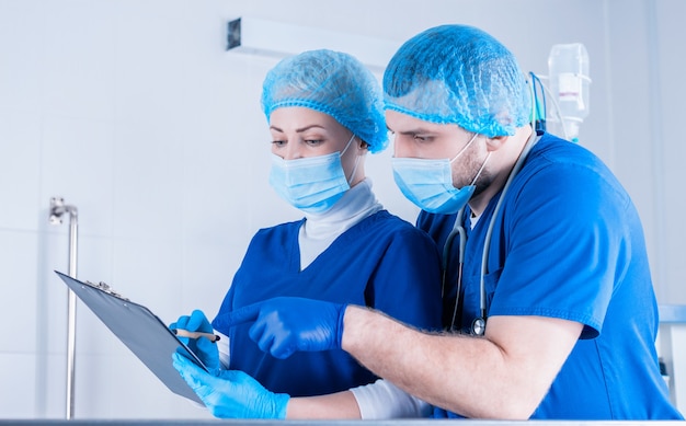 O cirurgião explica para a anestesiologista. e ela faz anotações no tablet