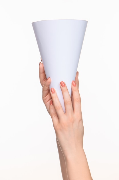 O cone branco dos adereços nas mãos femininas sobre fundo branco com sombra direita