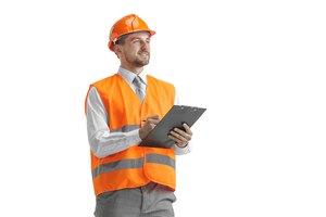 O construtor em um colete de construção e capacete laranja em pé no estúdio branco