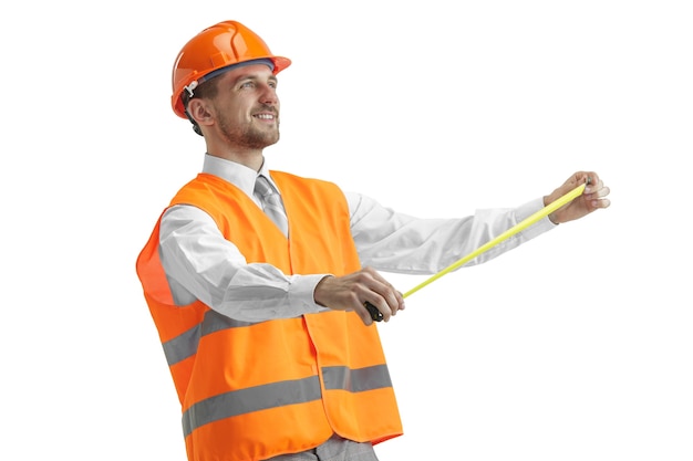 O construtor em um colete de construção e capacete laranja em pé no estúdio branco