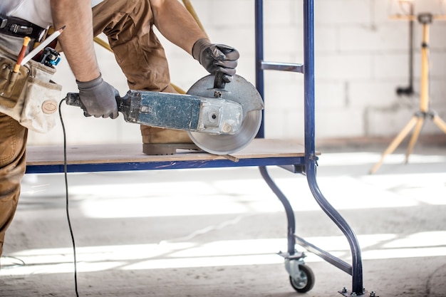 O construtor industrial trabalha com uma rebarbadora profissional para cortar tijolos e construir paredes internas