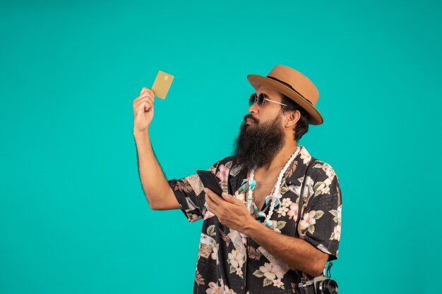 O de um homem de barba longa feliz usando um chapéu, vestindo uma camisa listrada, segurando um cartão de crédito dourado em um azul.