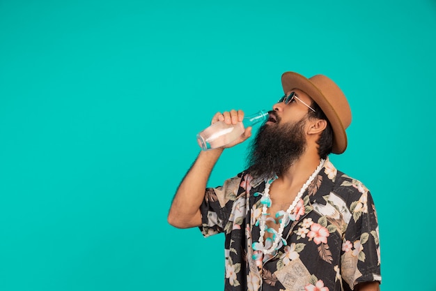 Foto grátis o de um homem feliz, com uma barba longa, usando um chapéu, vestindo uma camisa listrada, mostrando um gesto em um azul.