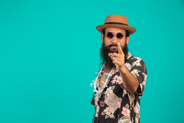 O de um homem feliz, com uma barba longa, usando um chapéu, vestindo uma camisa listrada, mostrando um gesto em um azul.